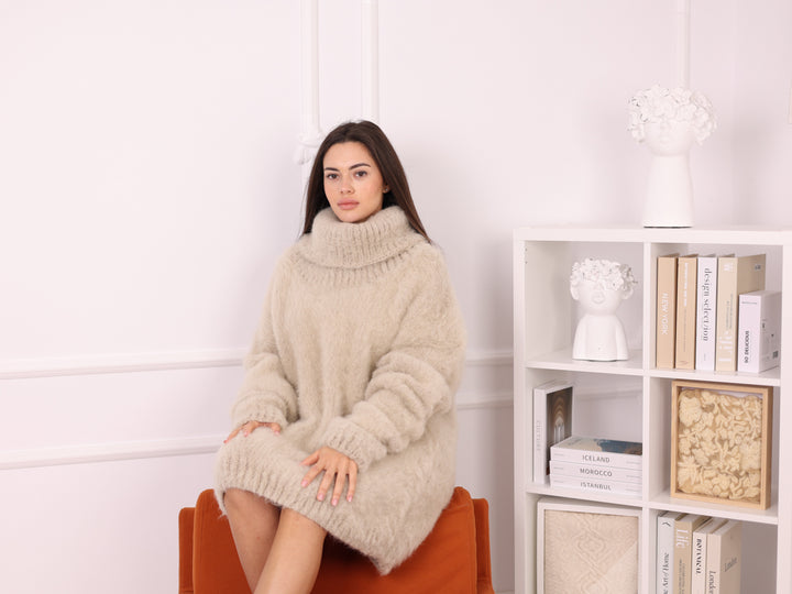 Woman wearing a beige oversized sweater sitting on an orange chair in a room with a bookshelf.