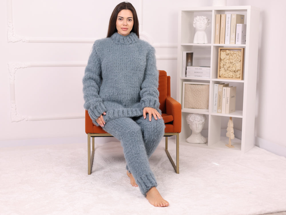 Woman wearing a blue knitted outfit sitting on an orange chair in a room with a bookshelf.