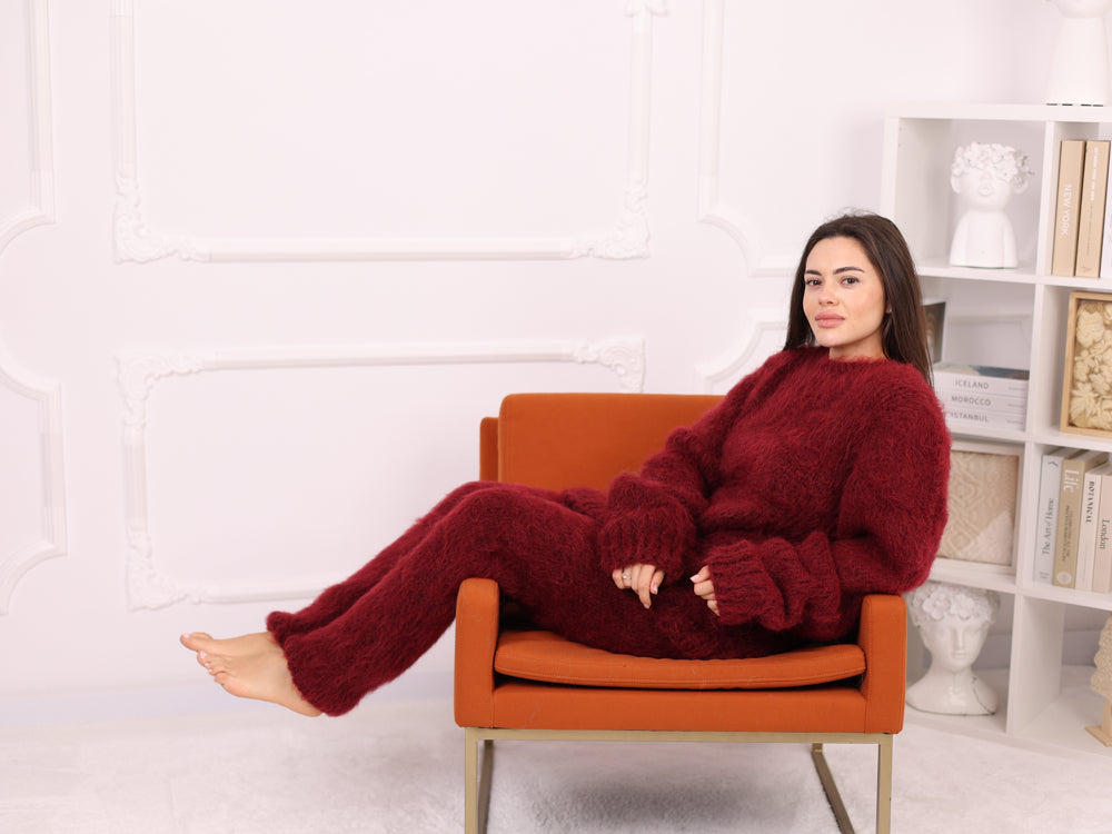 Woman in a red outfit sitting on an orange chair against a white wall with a bookshelf.