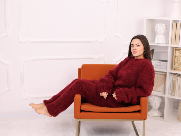 Woman in a red outfit sitting on an orange chair against a white wall with a bookshelf.