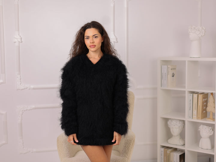 Woman wearing a black fluffy sweater in a room with a white wall and bookshelf.