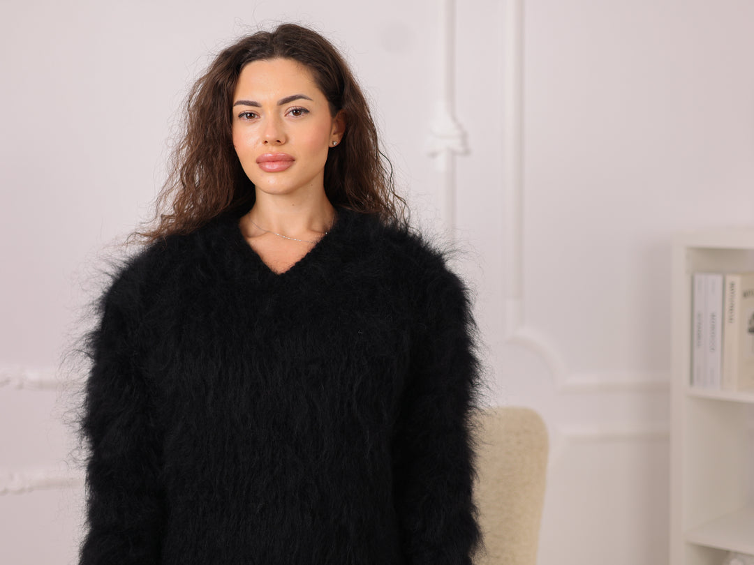 Woman wearing a black fluffy coat indoors against a white wall.