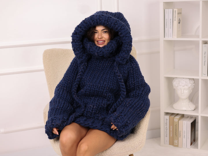 Woman wearing a large blue knitted sweater sitting on a chair.