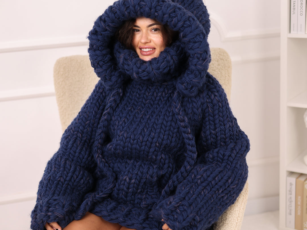 Woman wearing a large navy blue knitted sweater sitting on a chair.