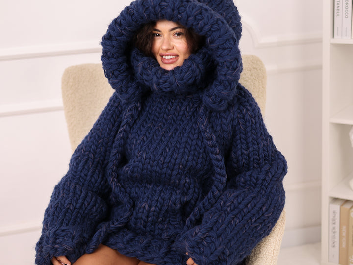 Woman wearing a large navy blue knitted sweater sitting on a chair.