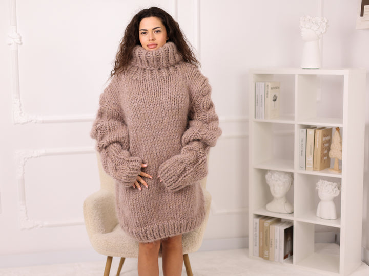 Woman wearing a large knitted sweater in a room with a white bookshelf.