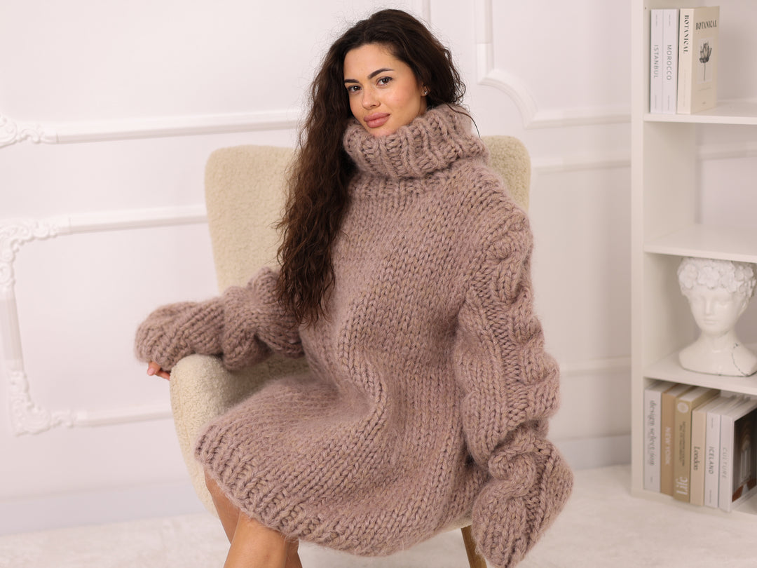 Woman wearing a large knitted sweater sitting on a chair in a cozy room.