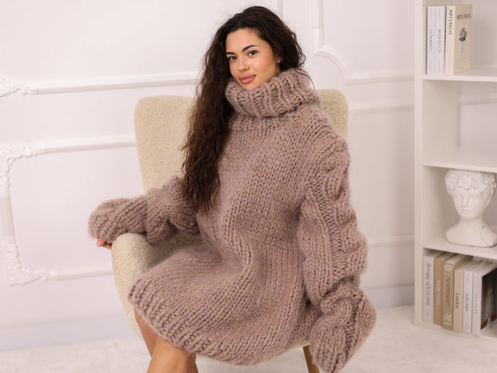 Woman wearing a large knitted sweater sitting on a chair in a cozy room.