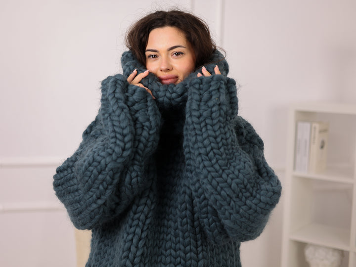 Woman wearing a large blue knitted sweater indoors.
