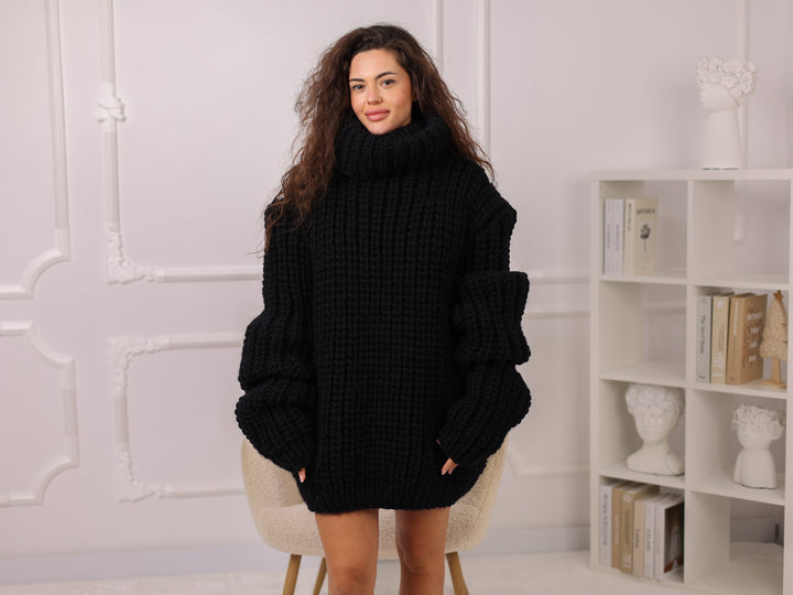 Woman wearing a black oversized sweater in a room with a white wall and bookshelf.