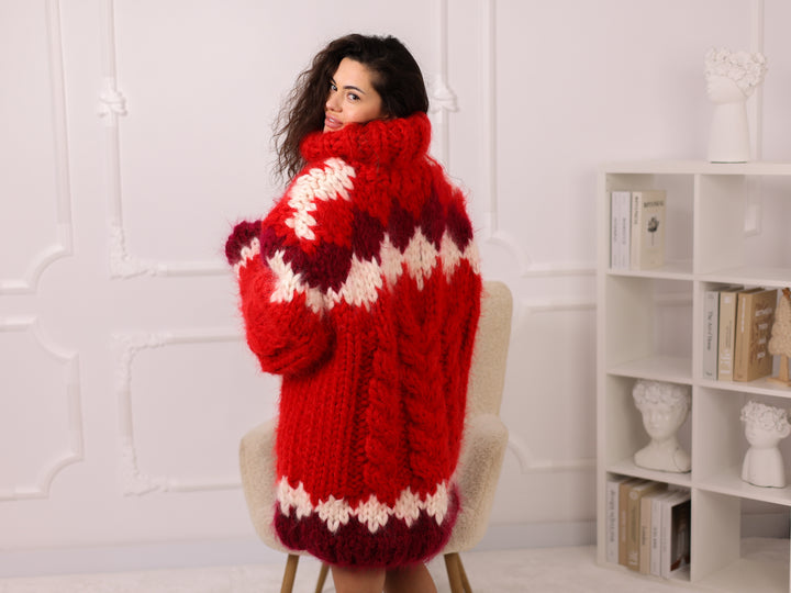 Woman wearing a red, white, and purple patterned sweater in a room with a white wall and bookshelf.