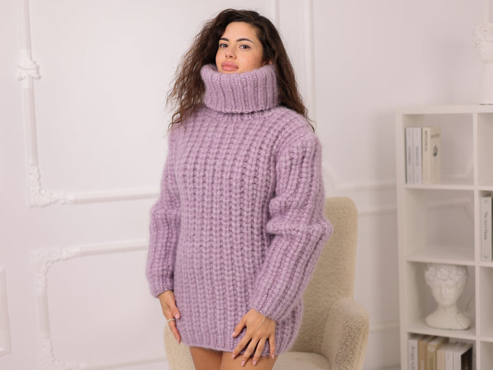Woman wearing a purple sweater dress in a room with a white wall and bookshelf.
