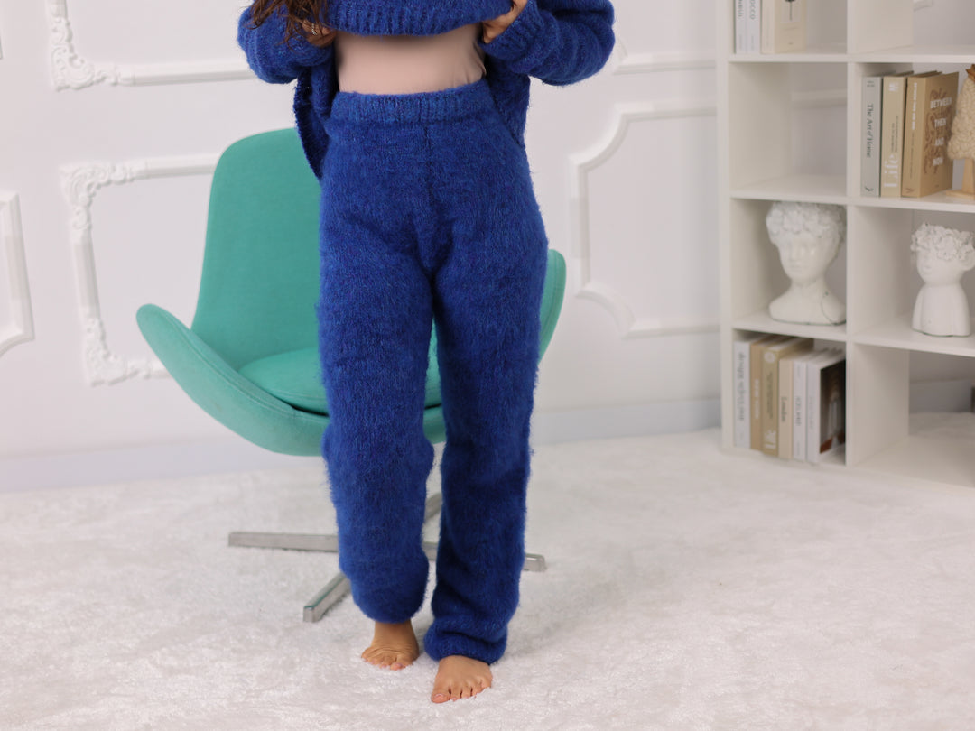 Person wearing blue fuzzy pants sitting on a green chair against a white brick wall.