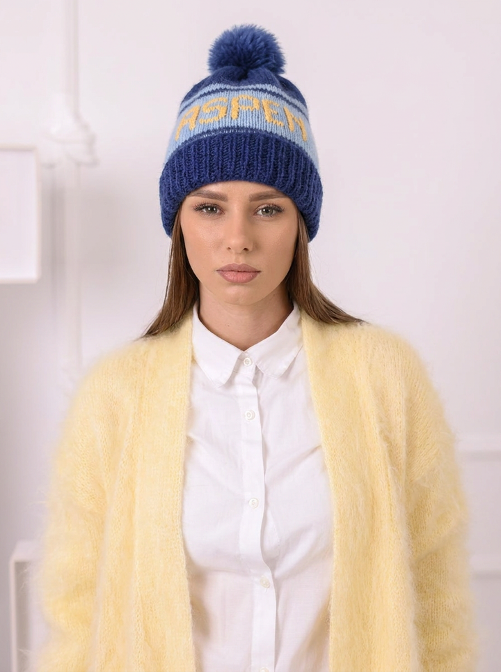 Woman wearing a blue knitted beanie with a pom-pom and a yellow cardigan.