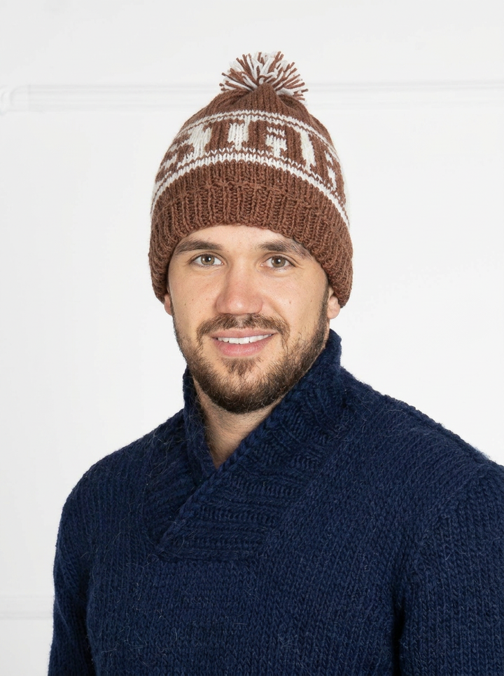 Man wearing a brown knit beanie with pom-pom and a navy sweater on a white background