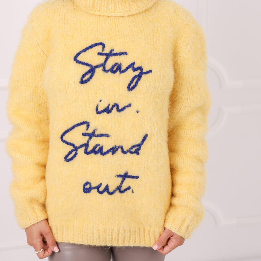 Close up of yellow alpaca sweater with embroidered text Stay in Stand out