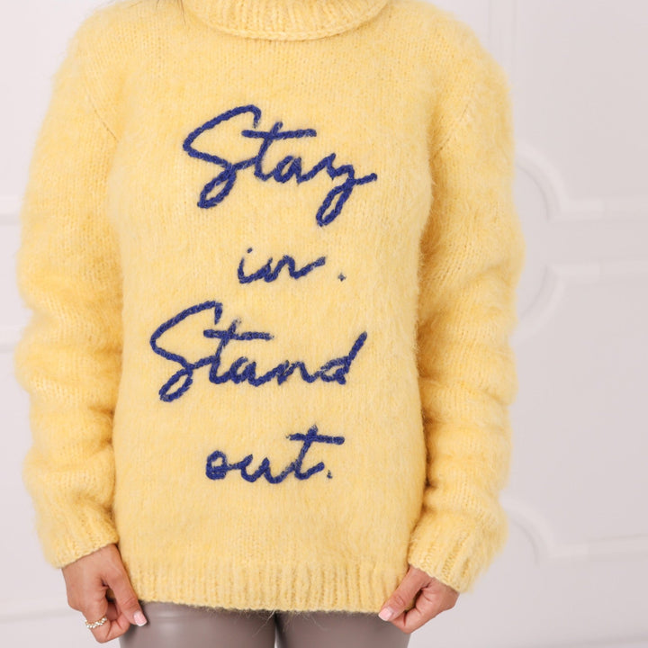Close up of yellow alpaca sweater with embroidered text Stay in Stand out